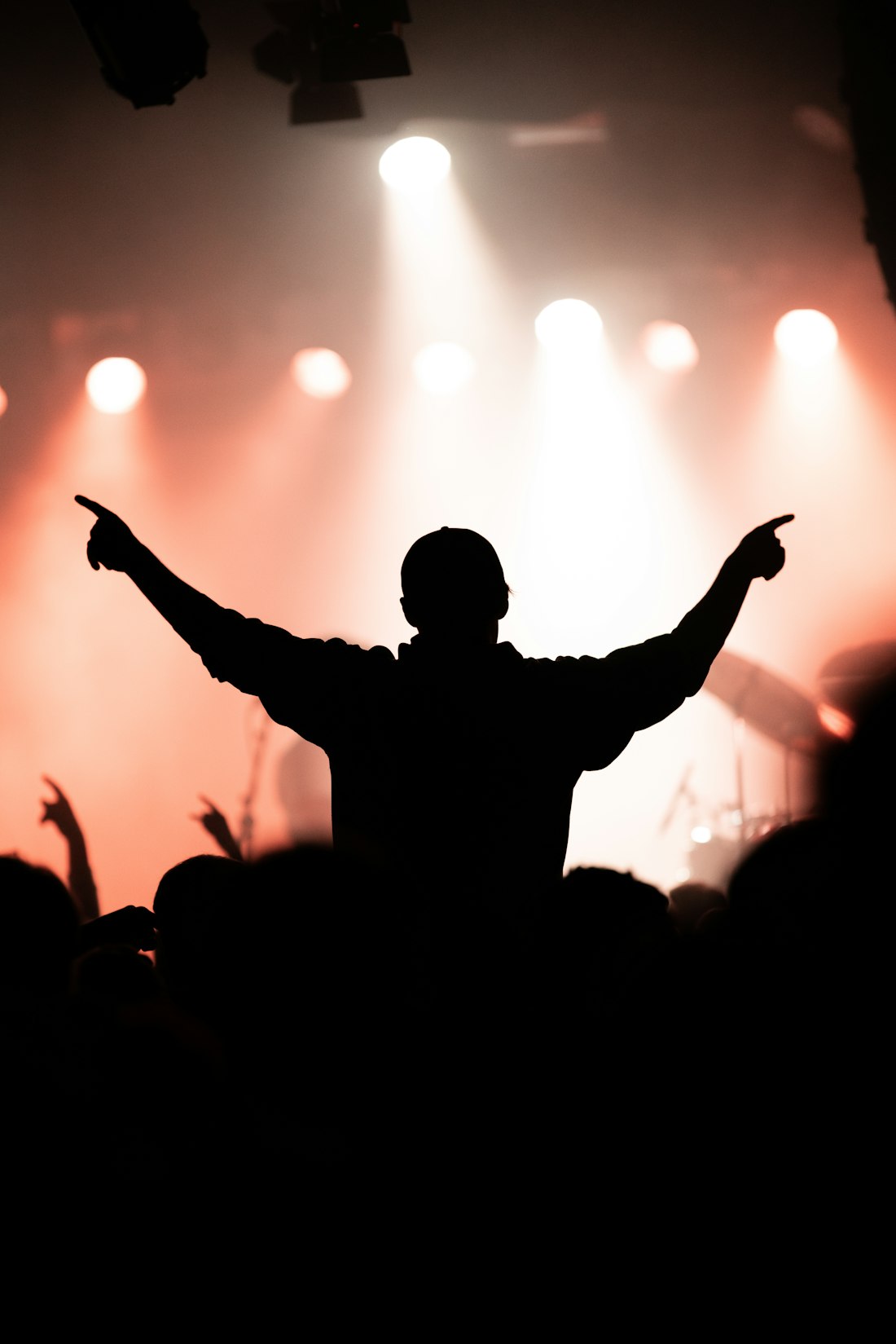 Silhouette of a fan with arms raised in front of a lit stage